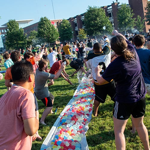 Crowd of students throwing water balloons on the green.