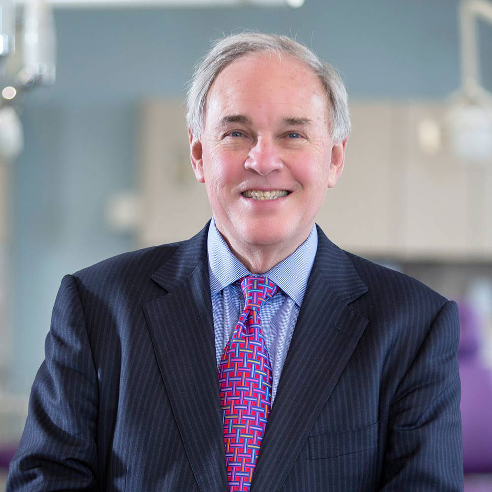 Benjamin J. Cumbus is a white man with gray hair, a dark jacket, light blue dress shirt, and vibrant fuschia patterned tie. 