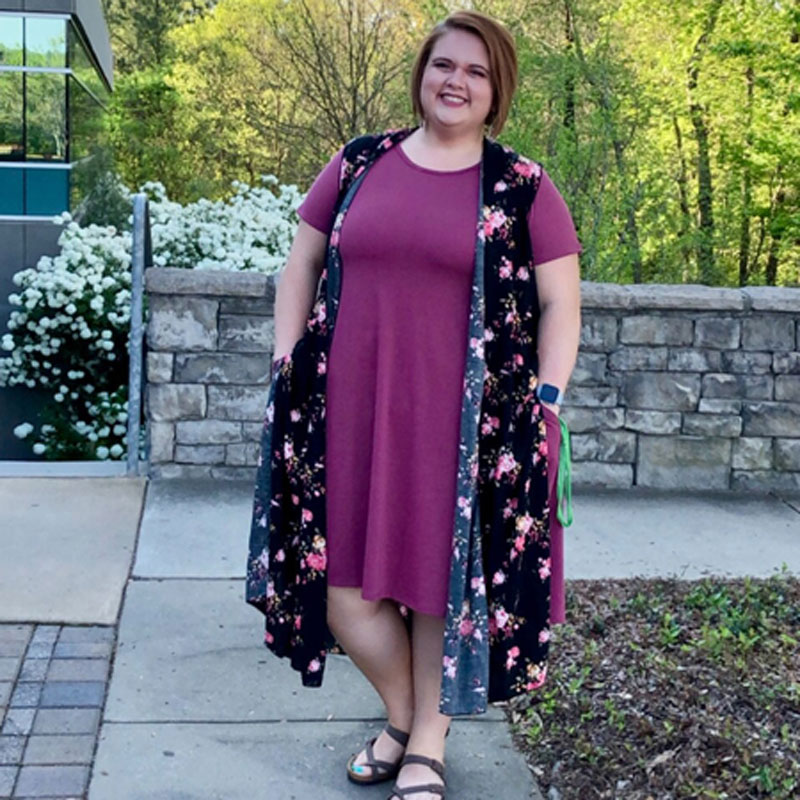 Jessica Wilson outside, wearing a plum dress and long black and pink vest.