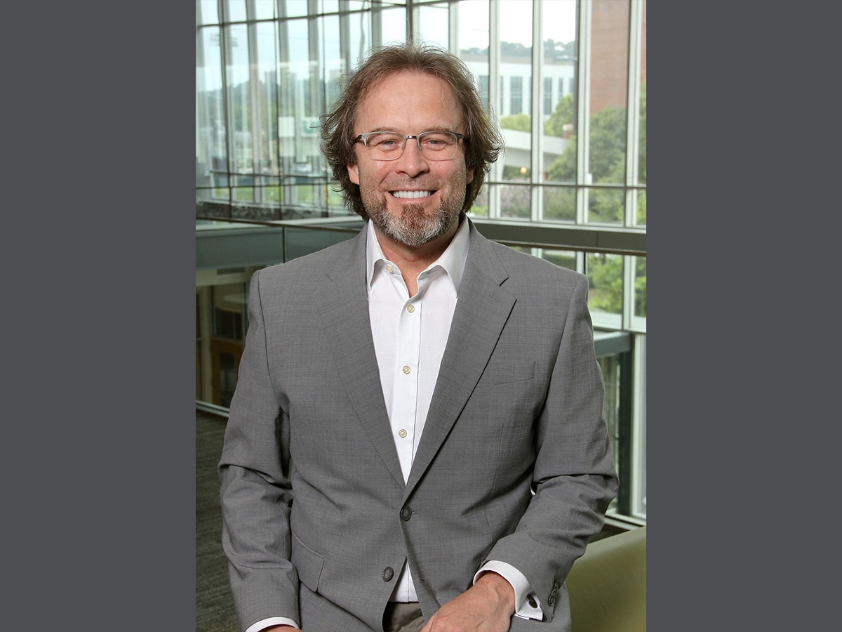 Smiling man with beard wearing a grey jacket, white shirt and glasses
