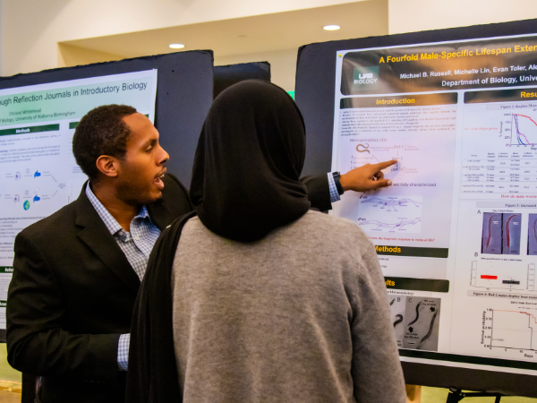 A graduate student presents his research to an onlooker 
