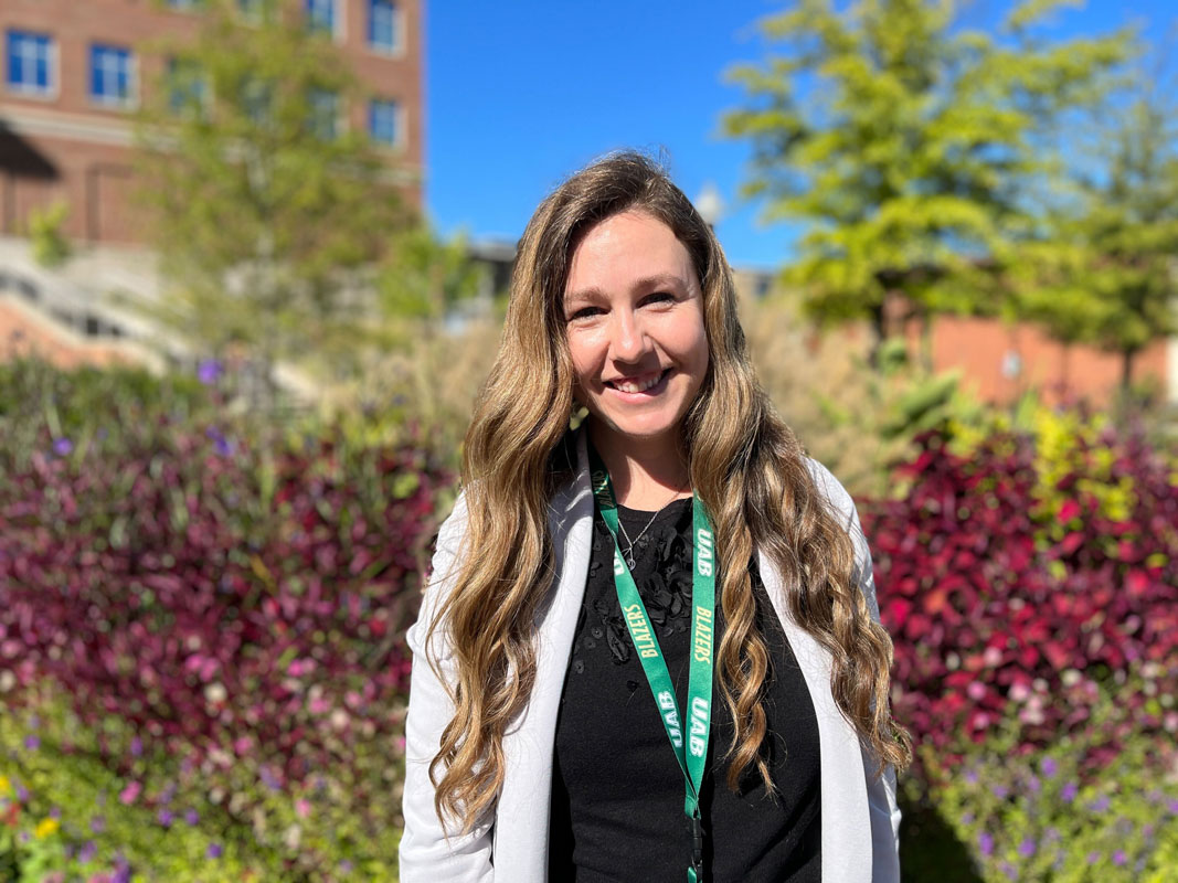 Lauren Wickman on the UAB campus, trees and colorful plants behind her.