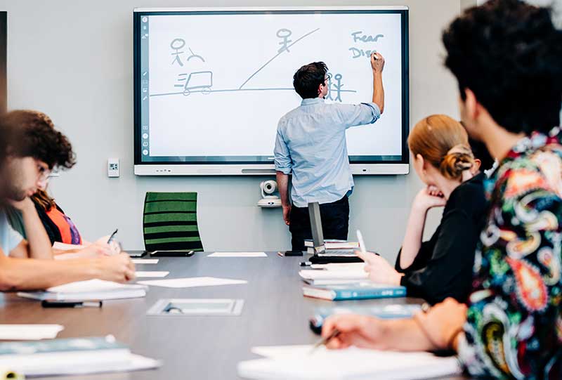 Photo of students in classroom with teacher writing on the board