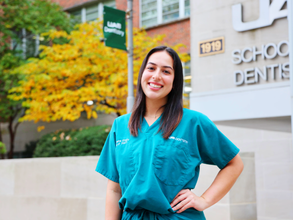 Cathereine Otano standing in front of UAB School of Dentistry building and UAB Dentistry Banner