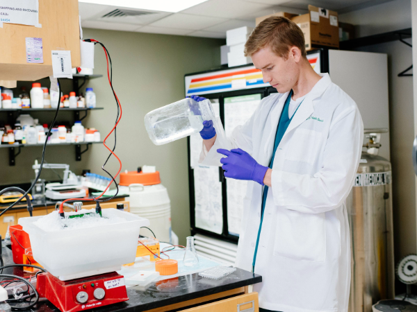 Tanner Godfrey pouring solution into beaker in a UAB SOD research lab