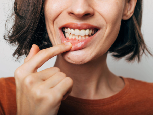 AdobeStock_543725614 Close up shot of gum inflammation Cropped shot of a young woman showing red bleeding gums isolated on a gray background Dentistry dental care By My Ocean studio