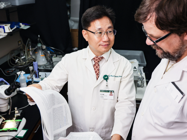 Man in white coat and glasses showing a research paper to a colleague  in a lab setting