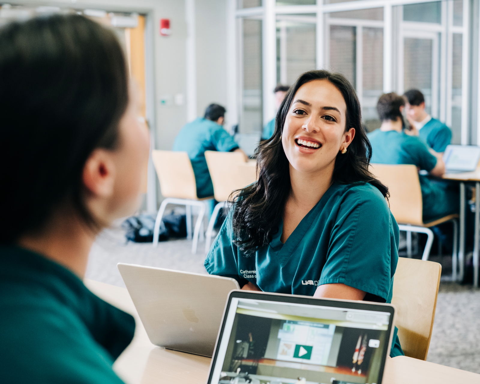 Two dental students on laptops in student lounge talking