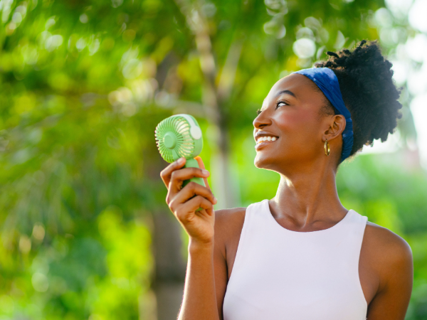 Young woman standing outside and smiling while holding a hand fan
