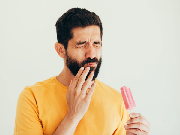 Man showing signs of sensitive teeth with ice cream on white background