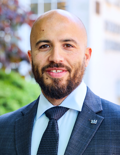 Man with bald head and brown beard wearing suit smiling for photo in front of the UAB School of Dentistry