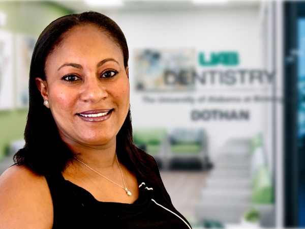 Smiling woman with dark hair and black top in front of blurred UAB Dentistry Dothan waiting area door