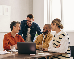 A group of smiling professionals gather around a laptop 