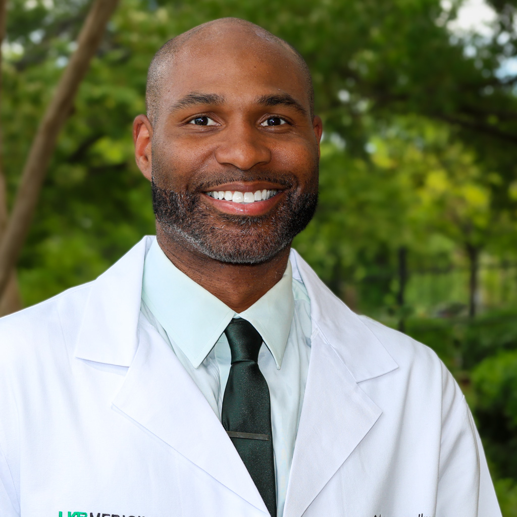 calvin spellmon smiles in front of a tree while wearing his white coats
