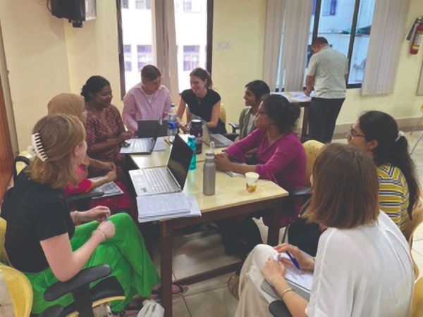 Group of people sitting around a table with laptops, collaborating during a global health meeting