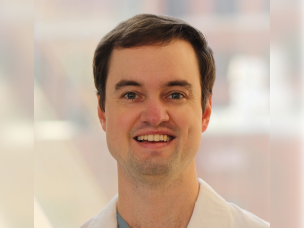 Professional headshot of Dr. Lee wearing a white clinical coat, centered against a softly blurred indoor background.