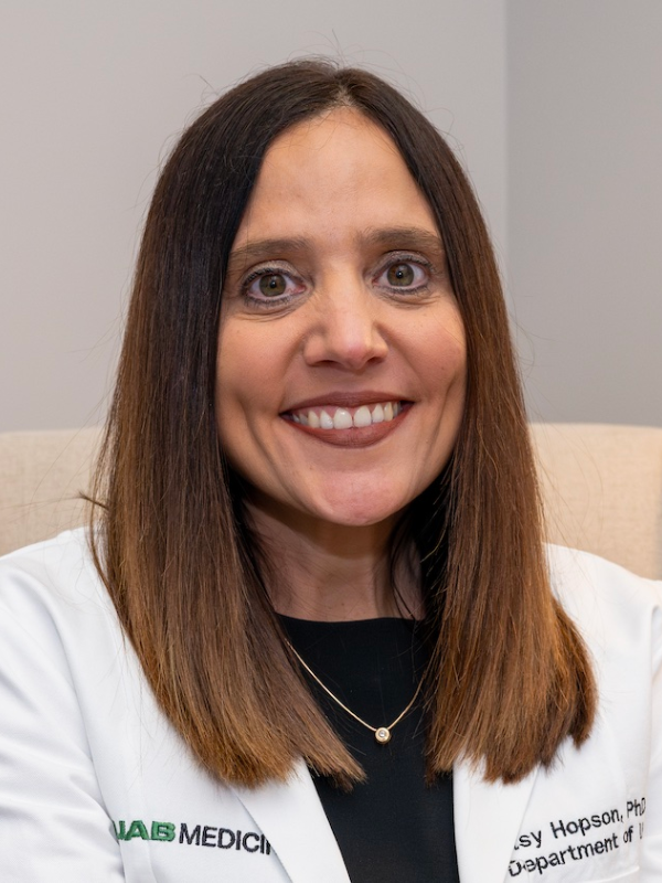 Betsy Hopson, Ph.D., stands in front of a gray wall.