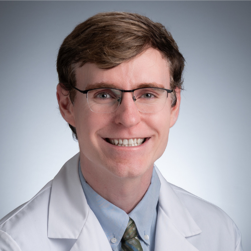 Headshot of a smiling blond male ophthalmologist wearing glasses and a white coat
