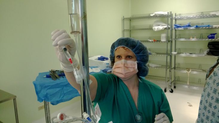 Dr. Carrie Atcheson in surgical scrubs and protective gear adjusts IV equipment in a clinical room.Provide your feedback on BizChat
