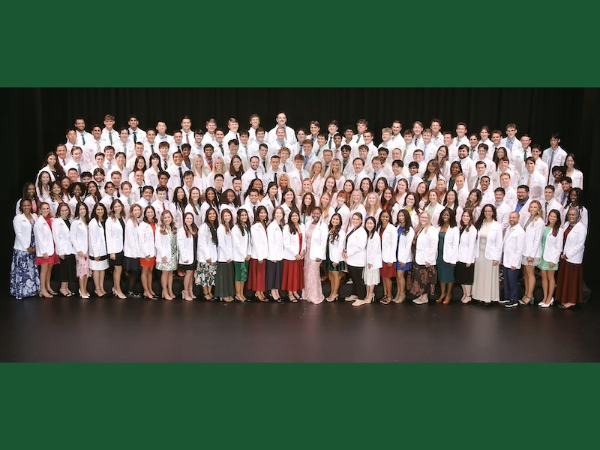 Group of medical students standing on a stage wearing medical white coats.