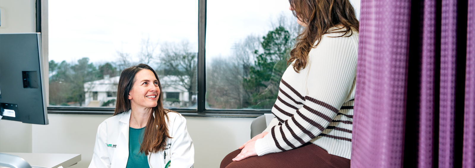Doctor is talking to a patient who is sitting on an examination table.