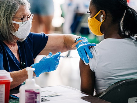 A female health care worker wearing a face mask is vaccinating a female student wearing a face mask against COVID-19 (Coronavirus Disease) by a health care worker at Bartow Arena, May 18, 2021.