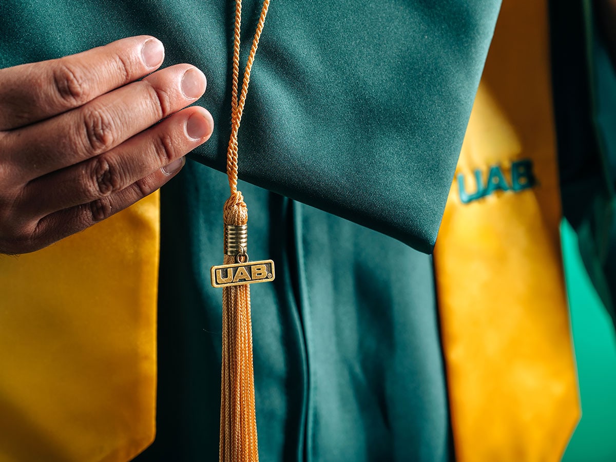Hand holding a UAB graduation cap with a UAB tassell
