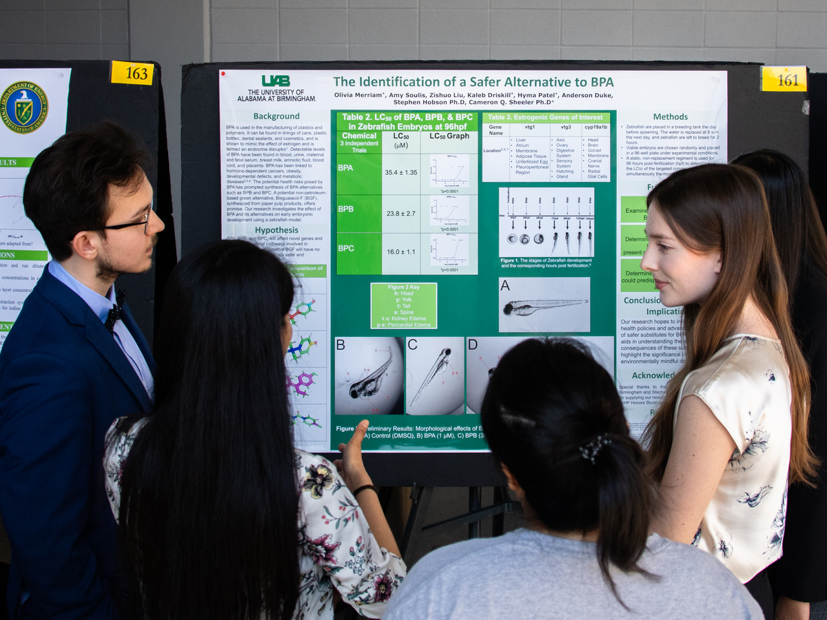 A student is speaking with others about the poster presentation of her research.