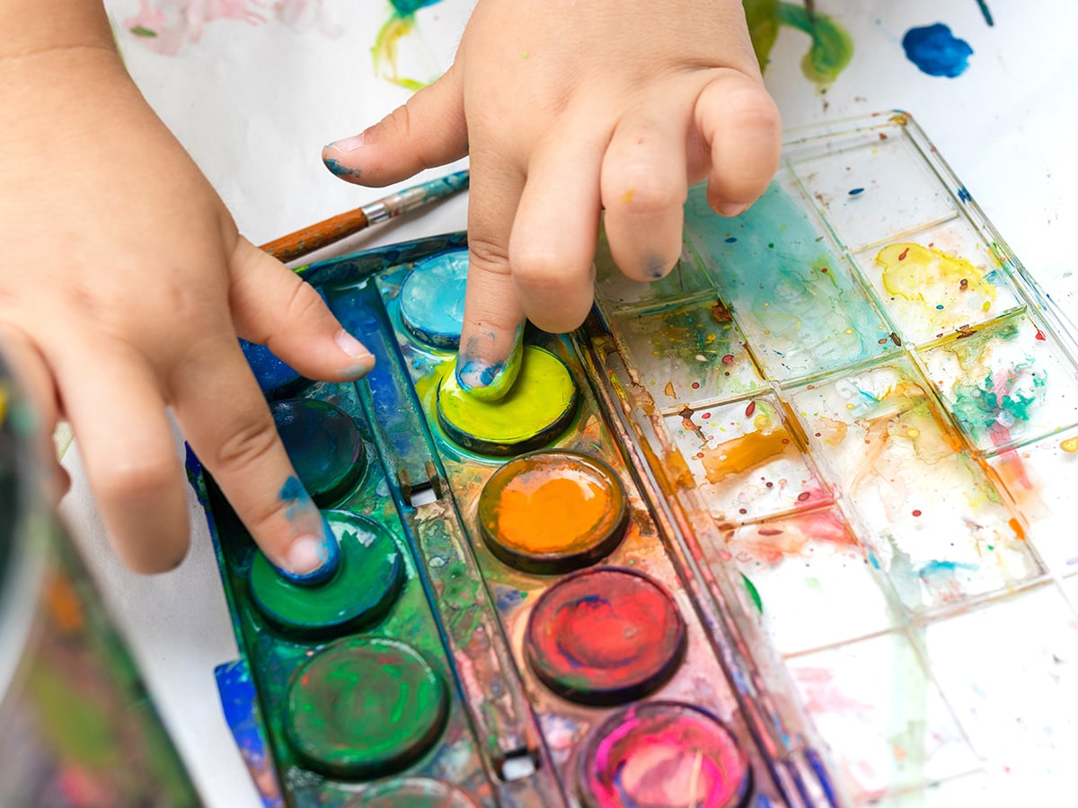 Child's hands touching the paint in a pallette