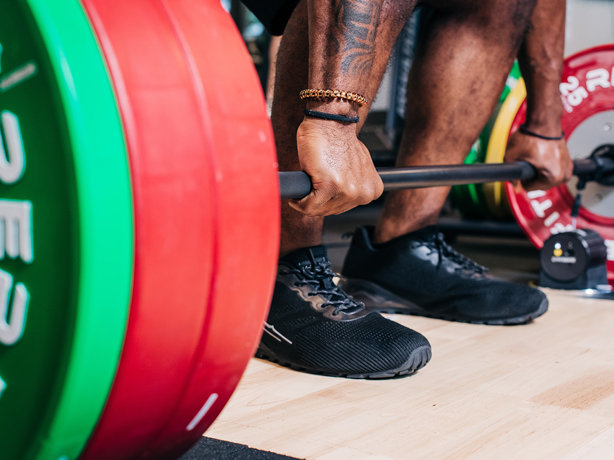Man prepares to lift weighted bar with 2 red 25 pound plates and 1 10 pound plate on each side.