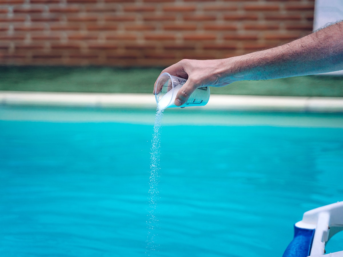 A man's arm shown adding chlorine powder to an outdoor pool