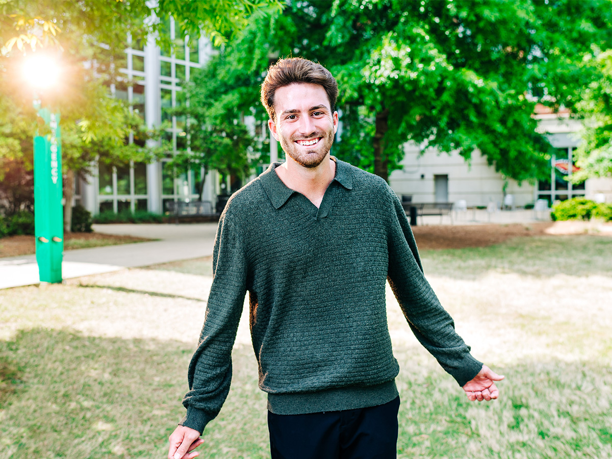 Photo of Josh Domingue in a green sweater in front of a tree.