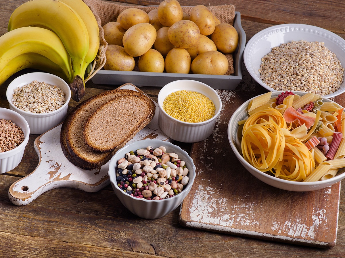 Wooden table with carbohydrates like potatoes, bananas, pasta, whole grains, beans, legumes and bread.