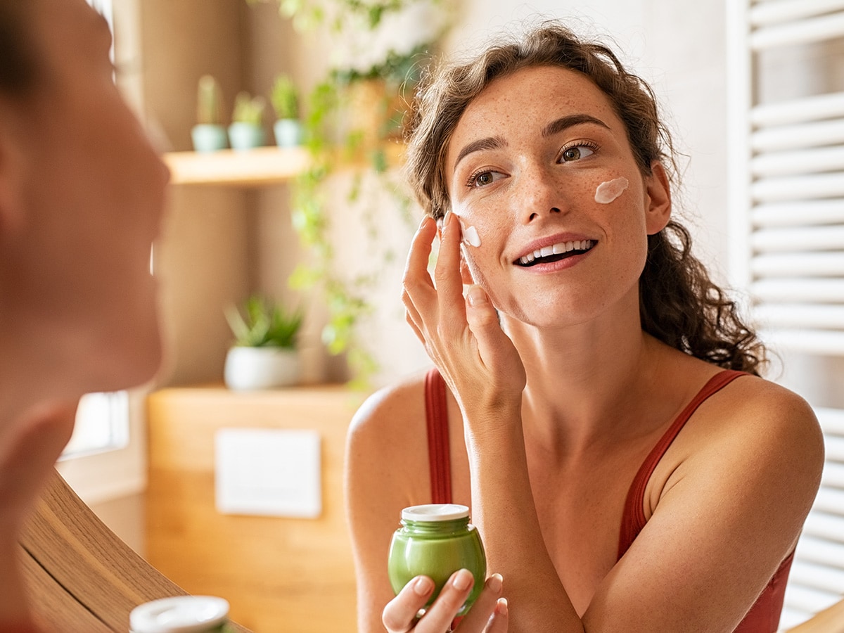 woman looking in the mirror applying moisturizer to her face