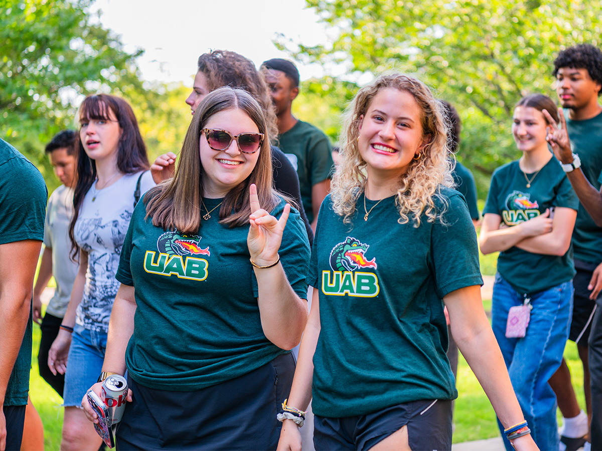 Two female freshmen UAB students in matching green shirts smiling at the camera. 