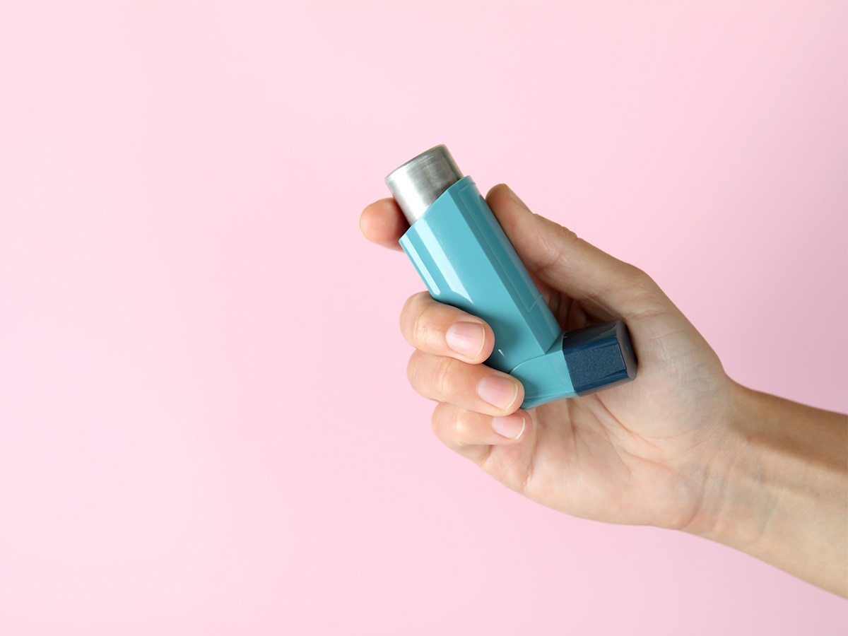 hand holding a blue inhaler with a pink background