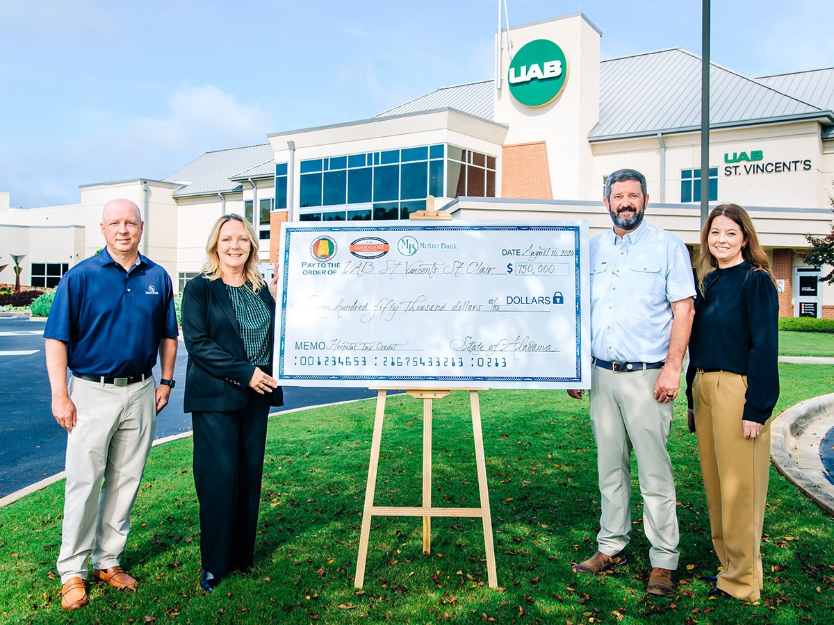  Group of people standing in front of a hospital holding a large check.