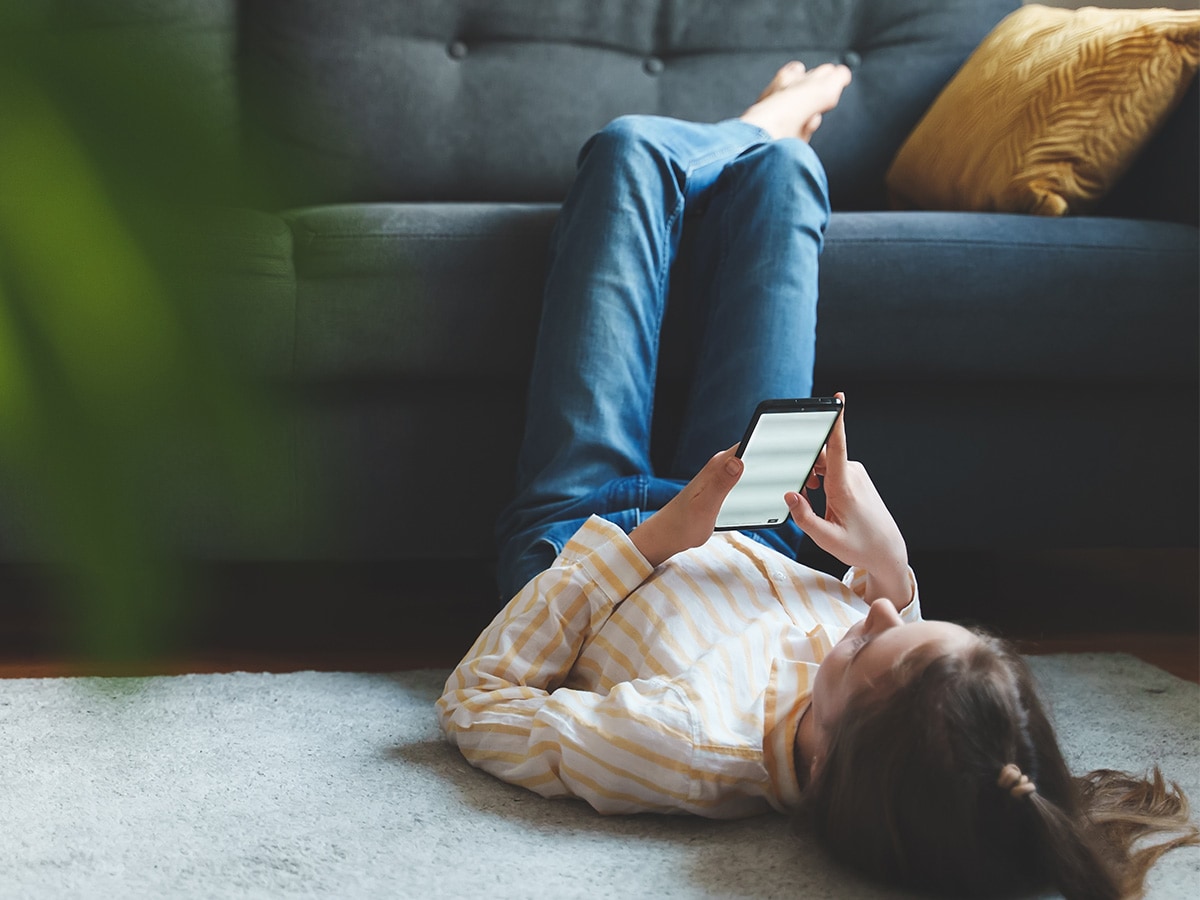 Tween girl with smartphone relaxing at home.