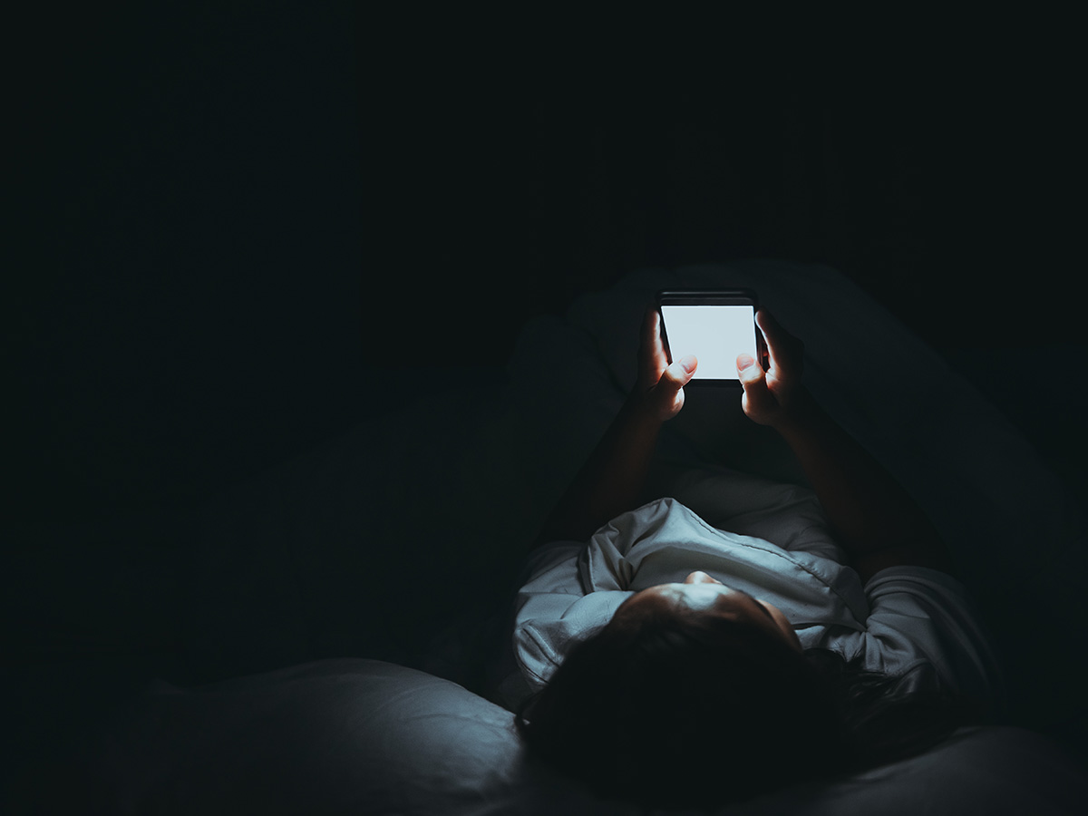 rep looking at phone in bed 1200x900px