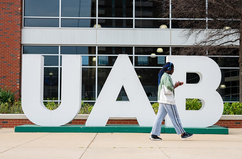 A student walks by large letters that spell U A B positioned in front of the Commons on the Green dining facility on UAB's campus