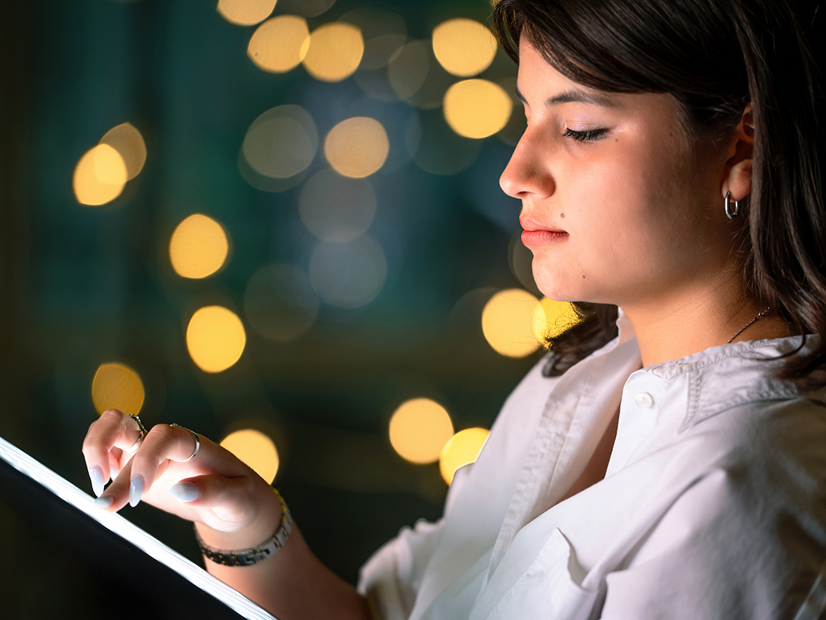 A student manipulates a tablet with glowing lights behind her in this staged image