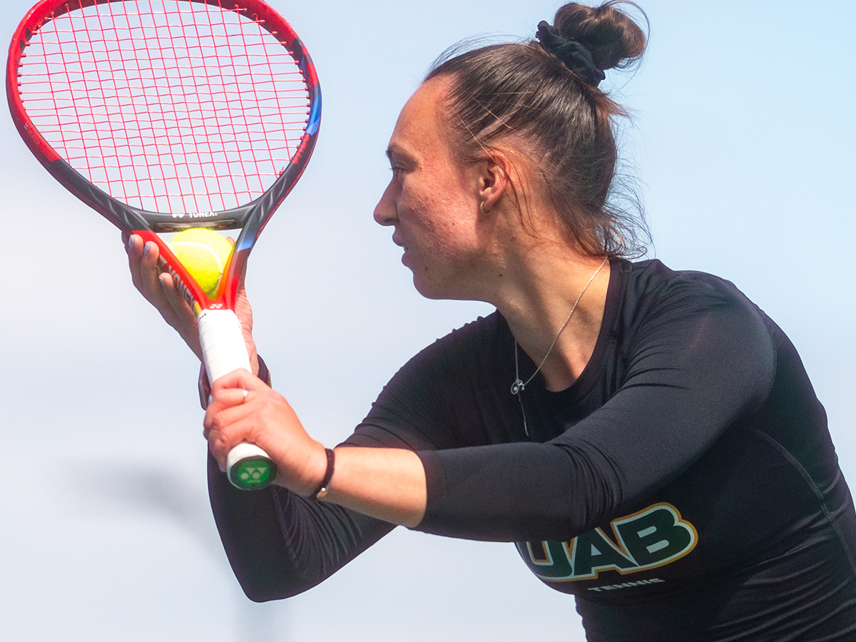 A UAB women's tennis player holds the ball and prepares to serve