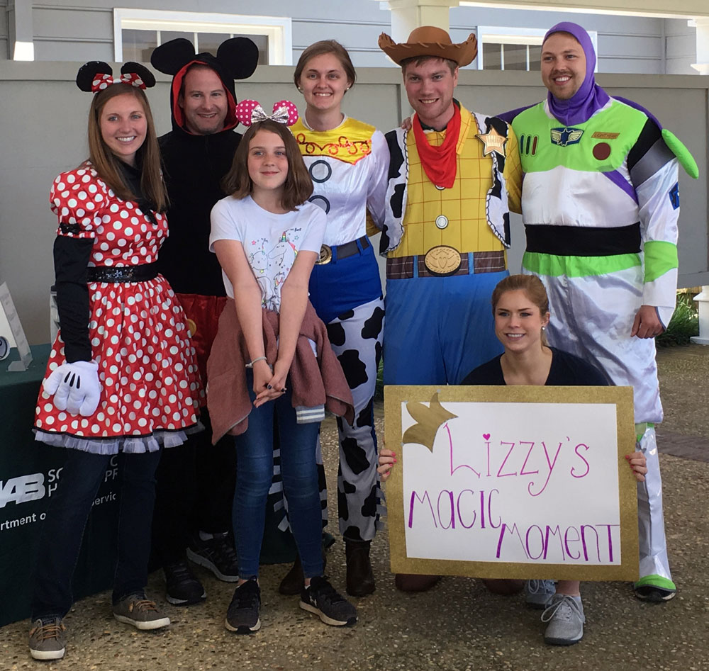 Lizxzy, a girl wearing Minnie Mouse ears, poses happily with people dressed as Minnie and Micky Mouse and lead characters from Toy Story. 