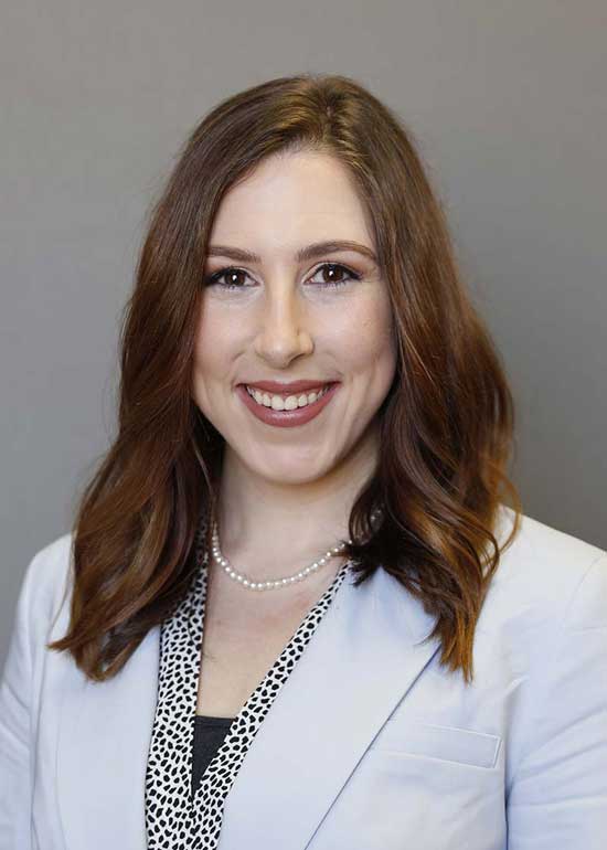 Christine Ferguson has long red-brown hair. She's wearing a white blazer and a black and white blouse. 