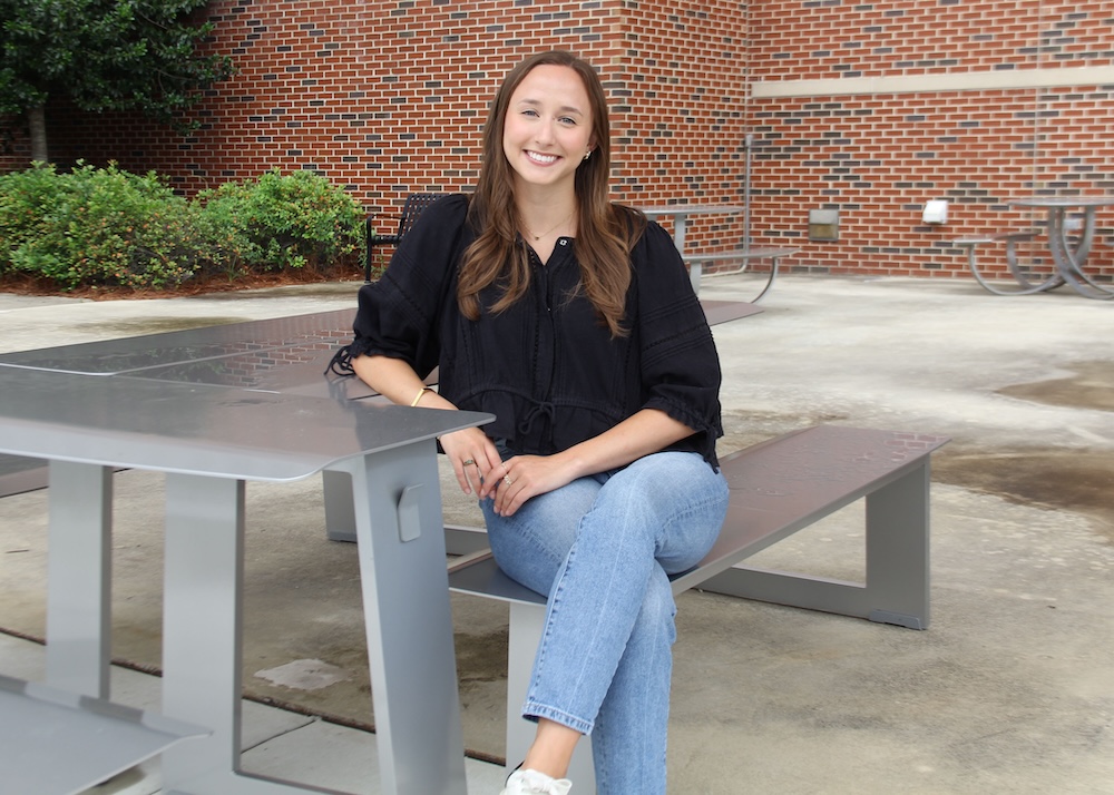Ellie Prados sits, legs crossed, at a table outside.
