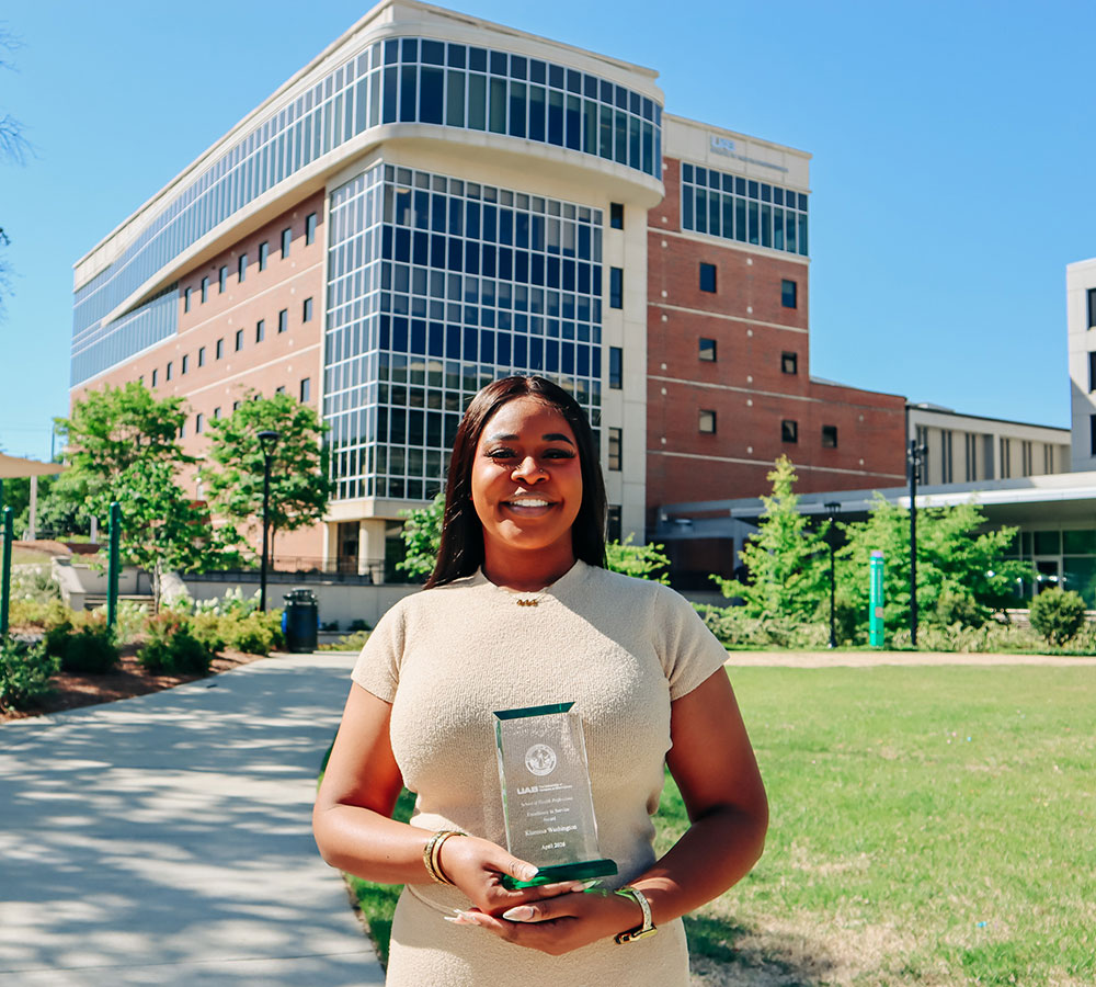 Washington holds her award outside the SHP building under a bright blue sky.