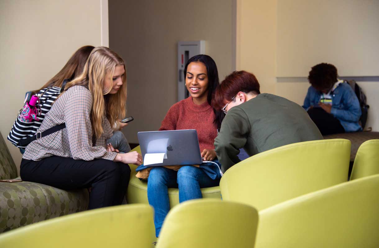 Students sitting in lounge looking at one girl's laptop.